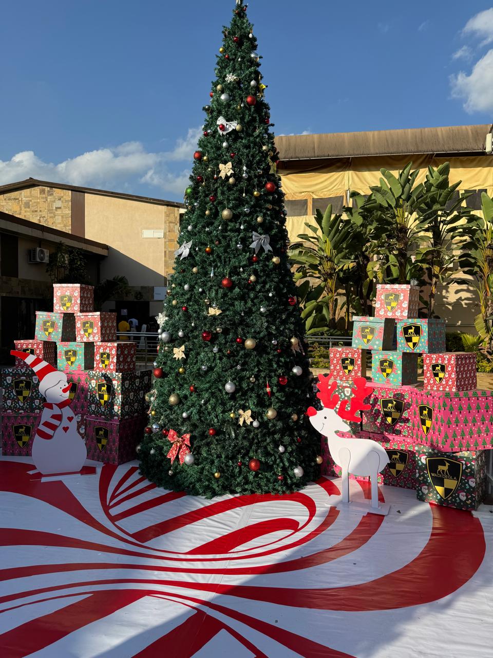 Decorated Christmas tree with a snowman, reindeer cutout and branded gift boxes on a peppermint-striped display base