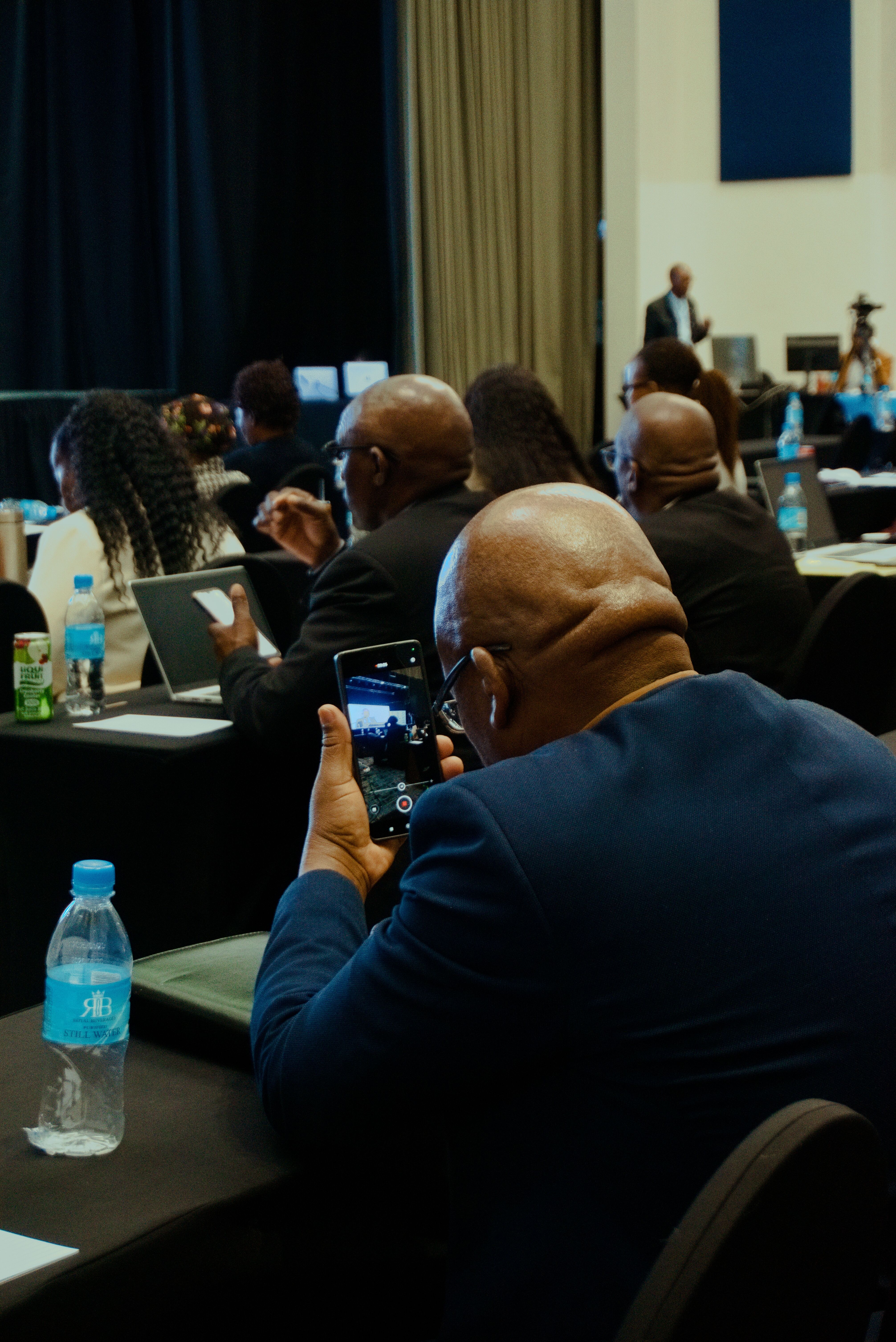 Representative image of conference delegates seated at tables, one capturing a presentation on his phone