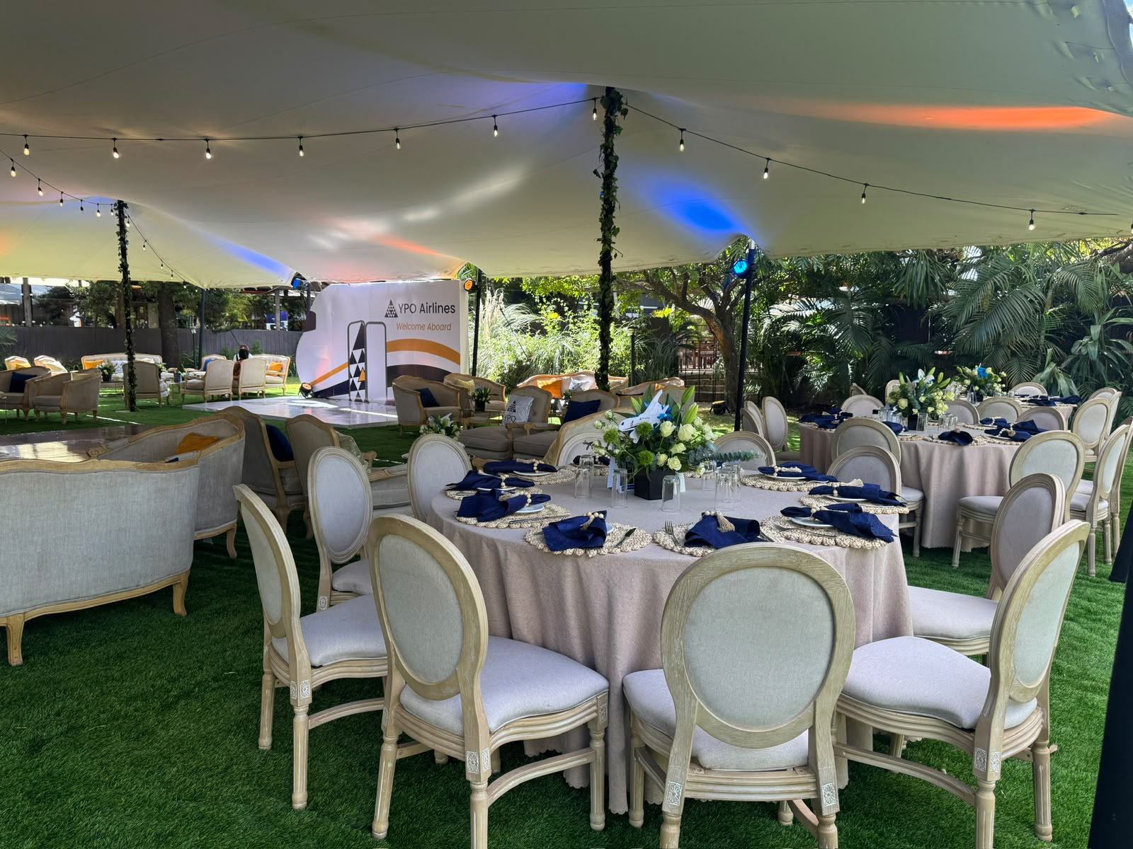 Tented outdoor gala with round tables, navy linens and a branded airline-themed backdrop stage
