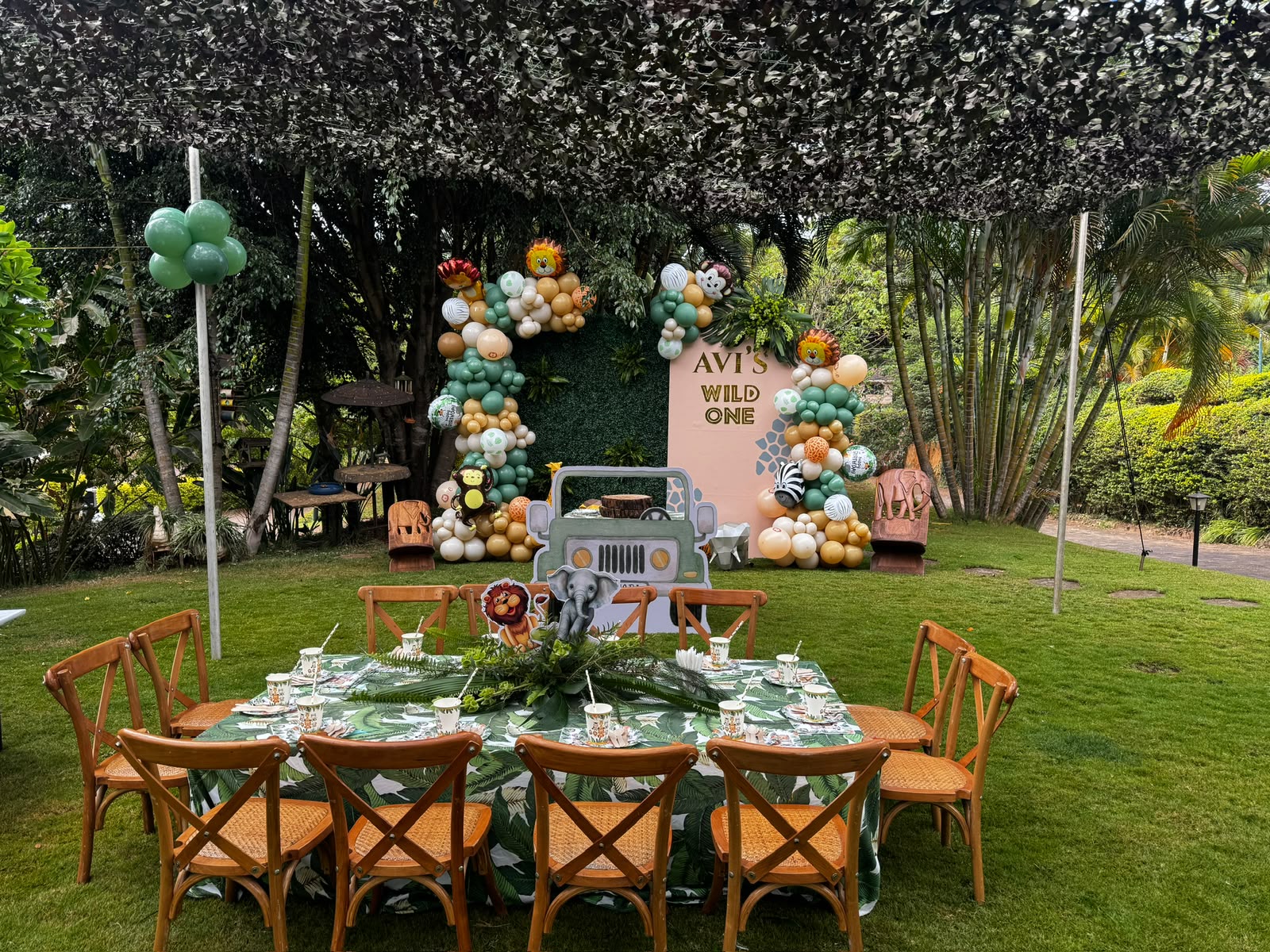 Safari-themed first birthday setup with balloon garlands, jeep cutout and jungle-leaf table linens