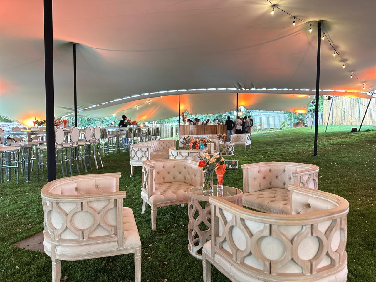 Sheer stretch tent with string lights over blush tufted lounge furniture on a lawn at dusk