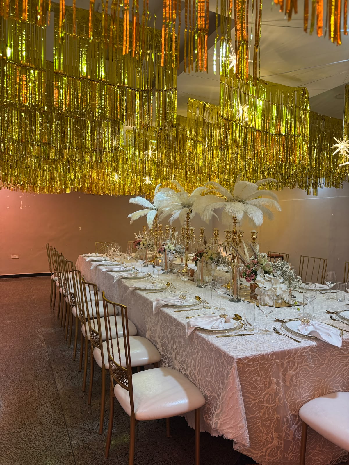 Luxury gala tablescape with gold candelabras, ostrich feathers and a shimmering gold fringe ceiling installation