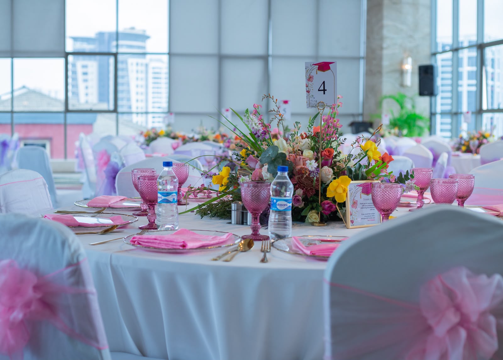 Elegant graduation tablescape with pink glassware, floral centerpiece and white chair sashes