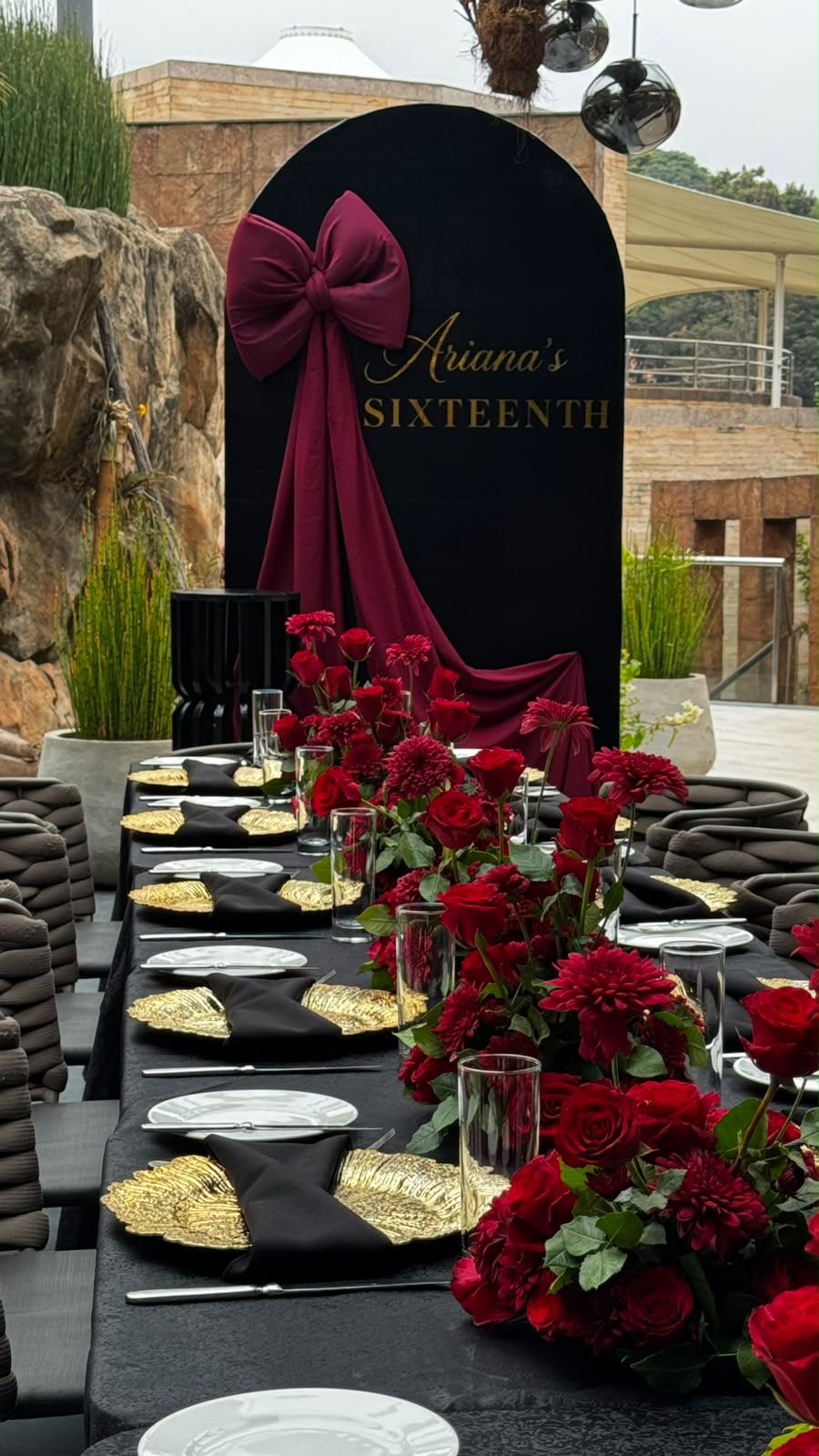Long table with black linens, gold leaf chargers and deep red rose and dahlia centerpieces